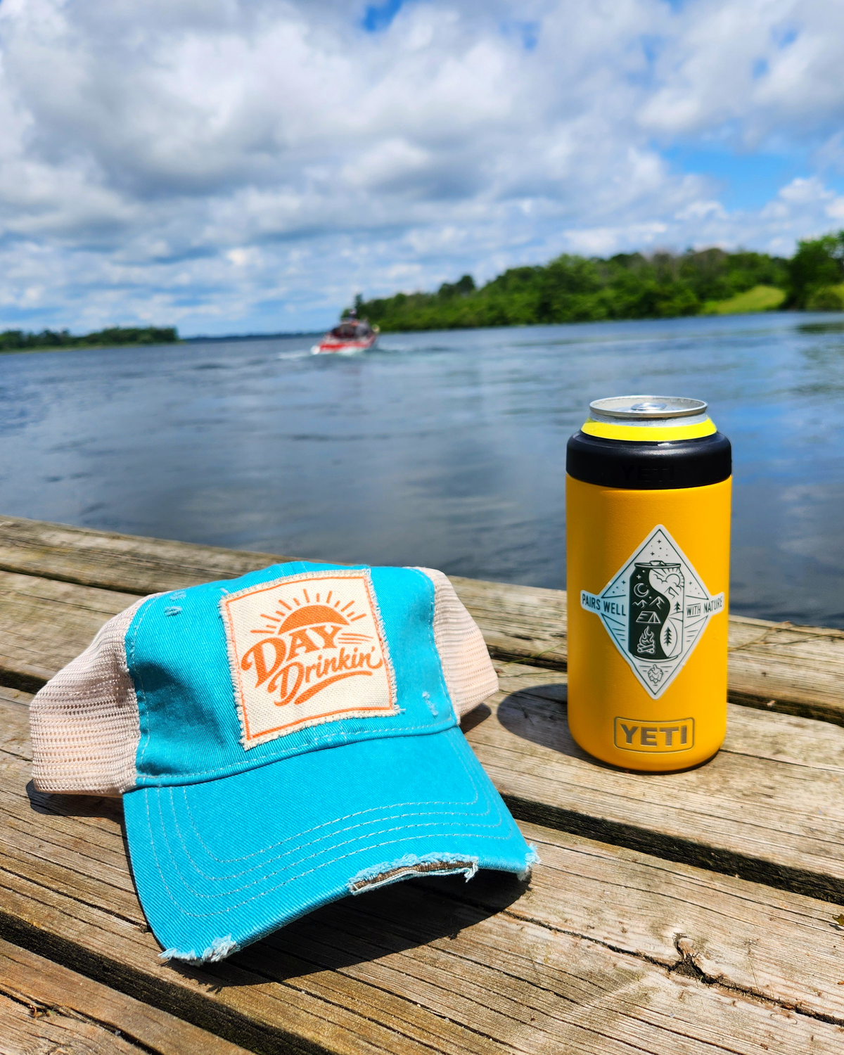 Day Drinkin' turquoise trucker hat on a dock beside the water, perfect for patio pints, summer adventures, and spontaneous afternoons